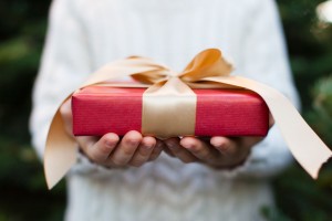 43693674 - close-up of nicely wrapped christmas gift being held by a child with no face visible, christmas tree in the background, christmas time concept